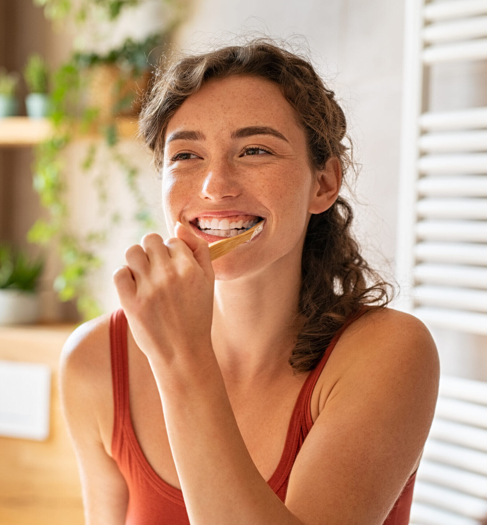 Smiling young woman brushing teeth in bathroom. Portrait of happy girl looking in mirror while using ecological toothbrush with whitening toothpaste. Beauty girl in bathroom cleaning teeth in the morning time.