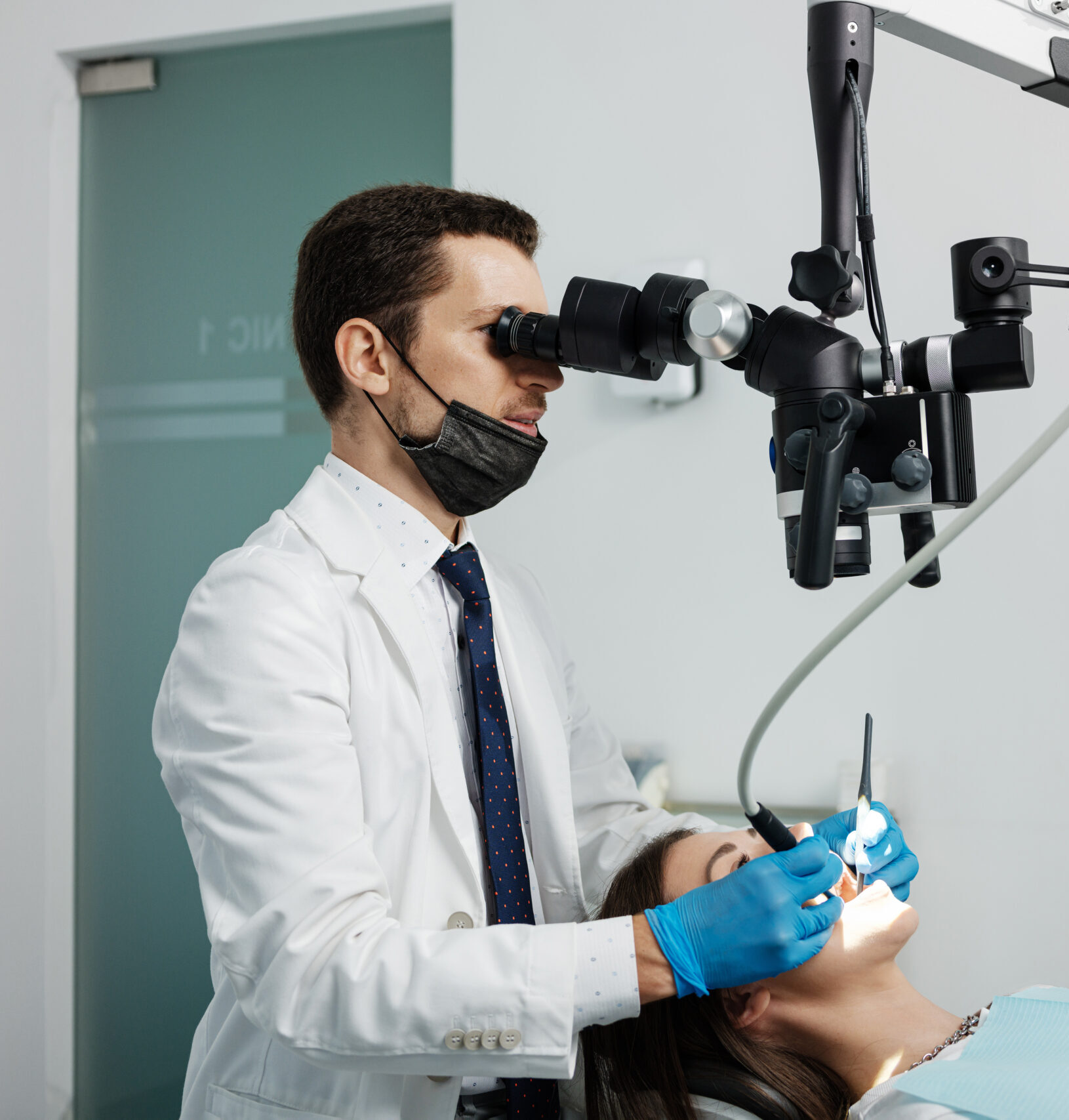 Male dentist using dental microscope treating female patient teeth at dental clinic office. Medicine, dentistry and health care concept. Dental equipment